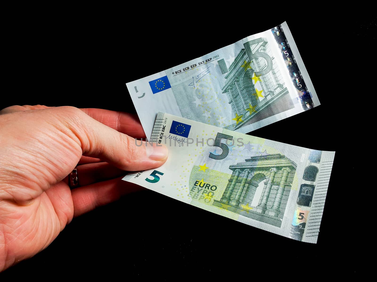 Old and new five Euro bills held by a male towards black background