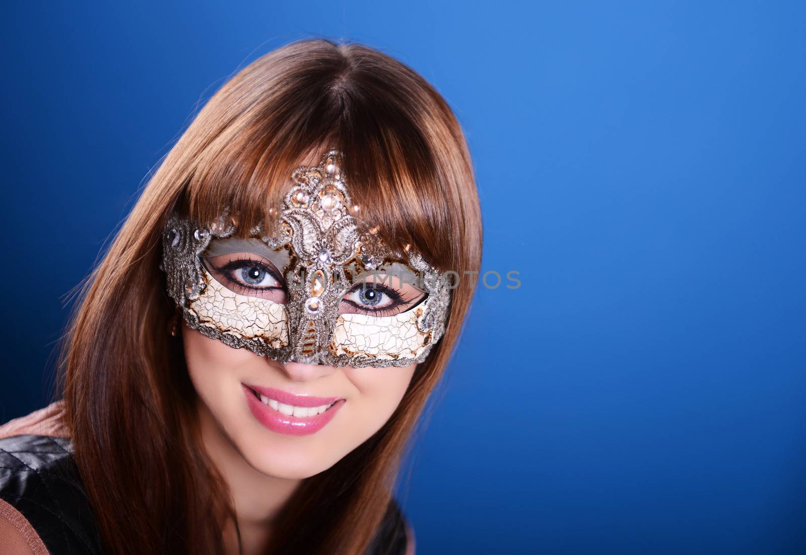 Beautiful caucasian brunette in carnival mask over blue background