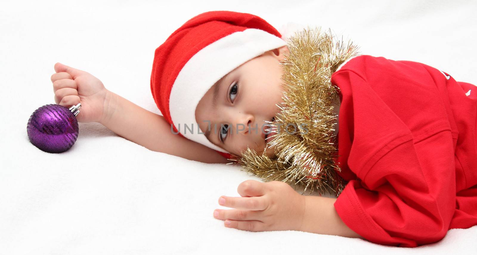 child in santa claus hat lies on bed by NikolayK