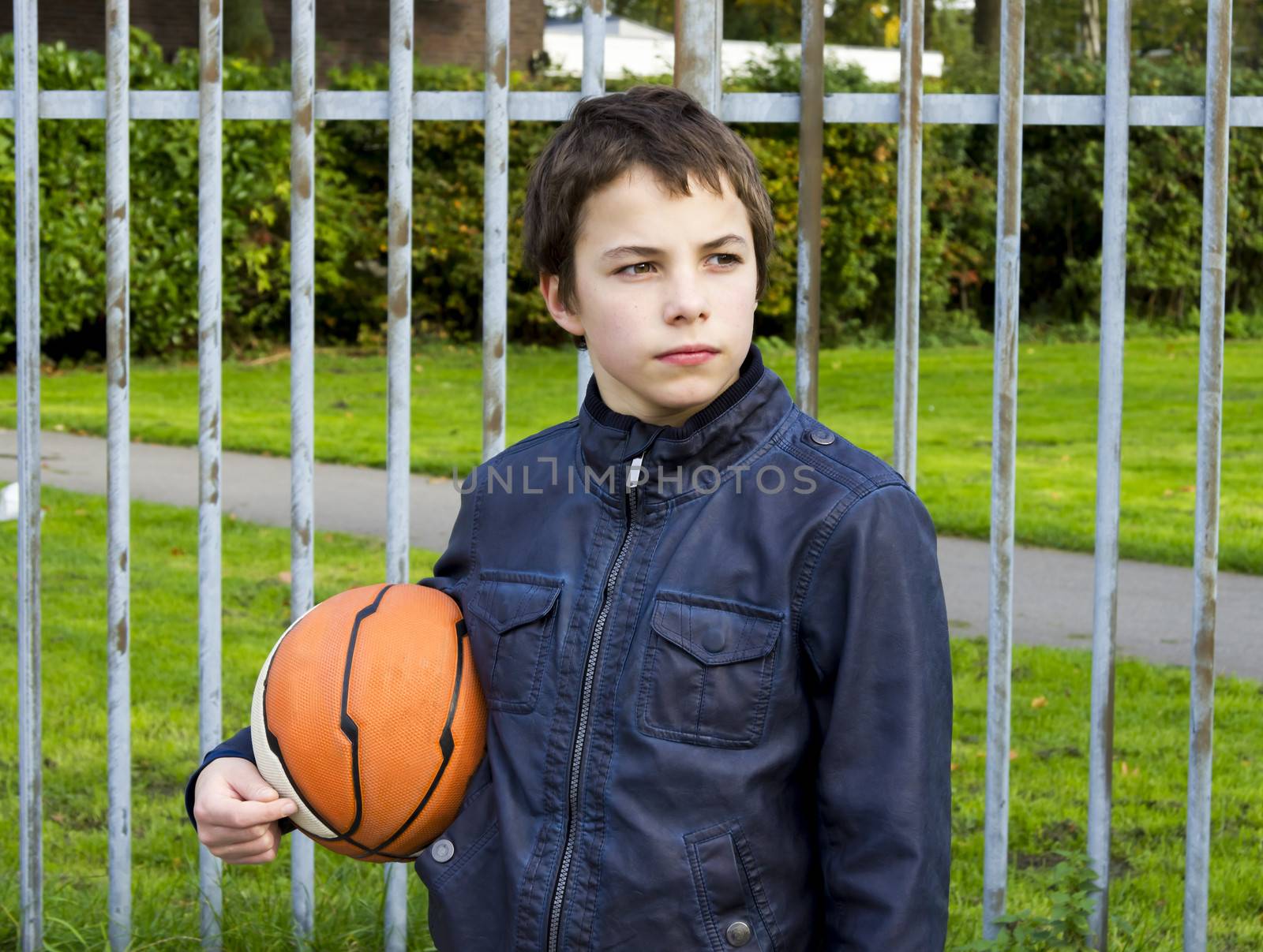 young basketball player holding ball against iron fence at the playground