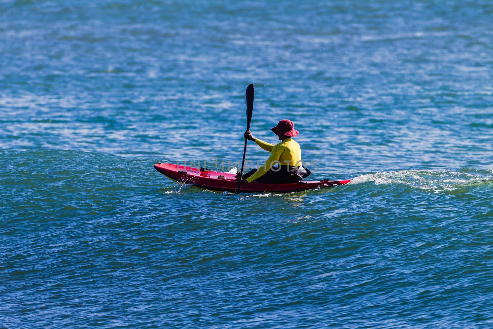 A man in a red hat rowing a red canoe in the ocean with a yellow life jacket on.