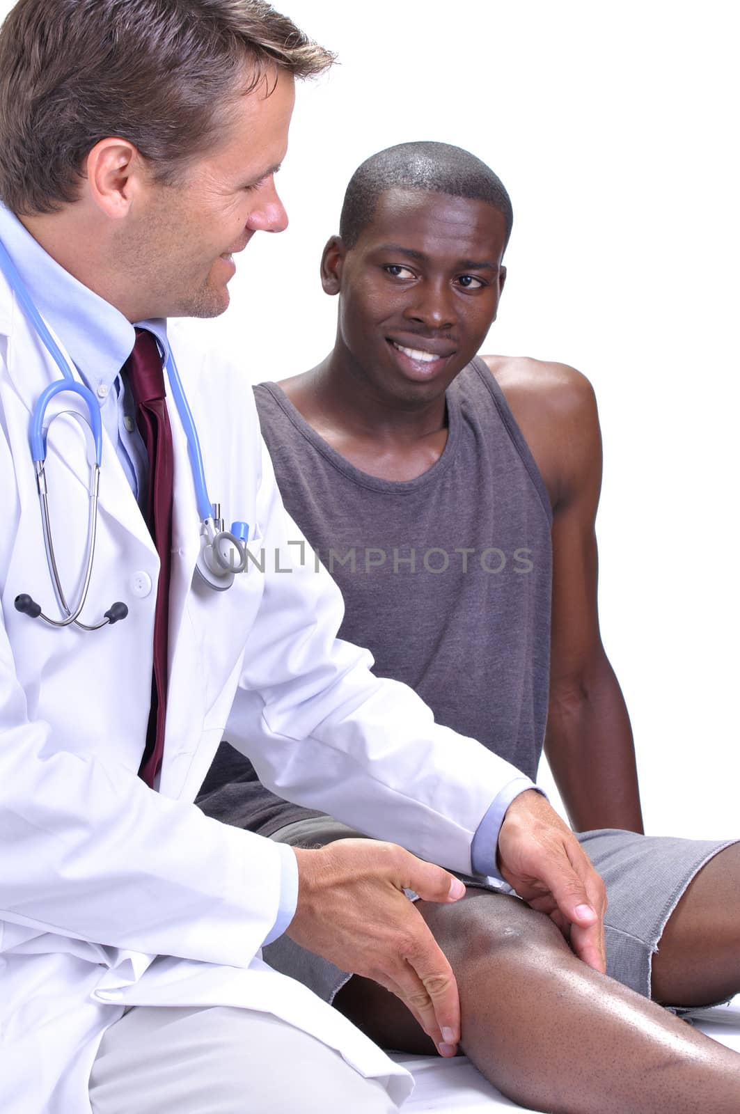 Medical doctor feels and checks the knee of his young athletic patient while they exchange a smile on white background