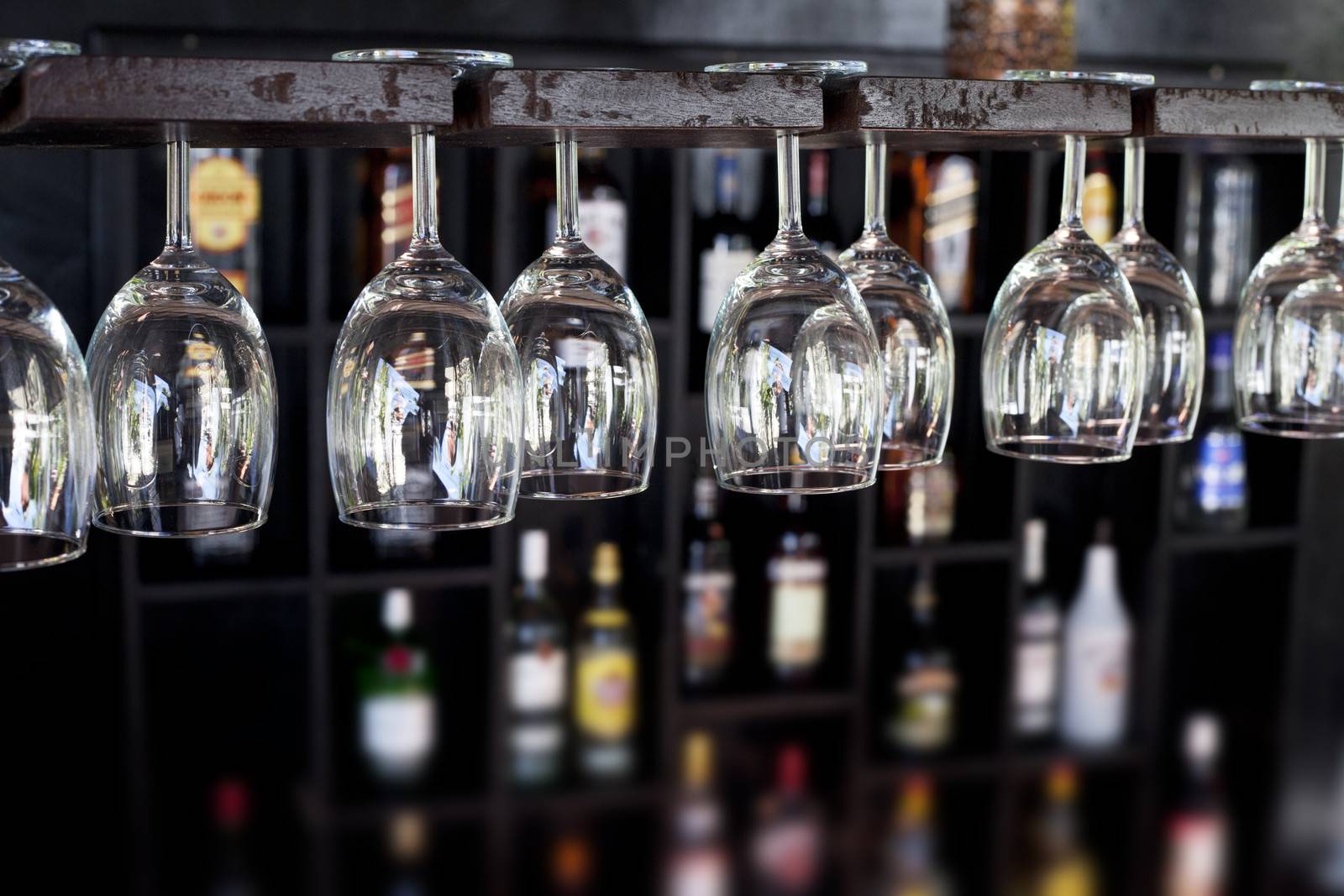 Wine glasses hanging upside down in a bar with bottles blurred in the background