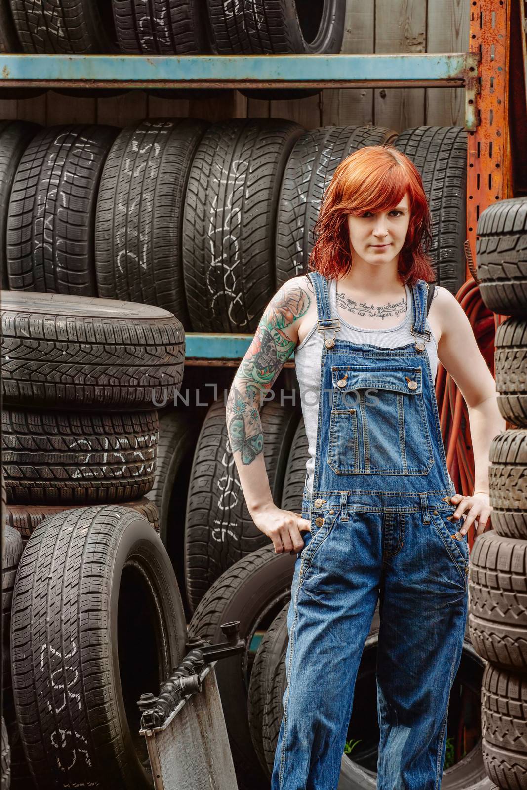 Photo of a young beautiful redhead mechanic wearing overalls and standing in an old garage. Attached property release is for arm tattoos.
