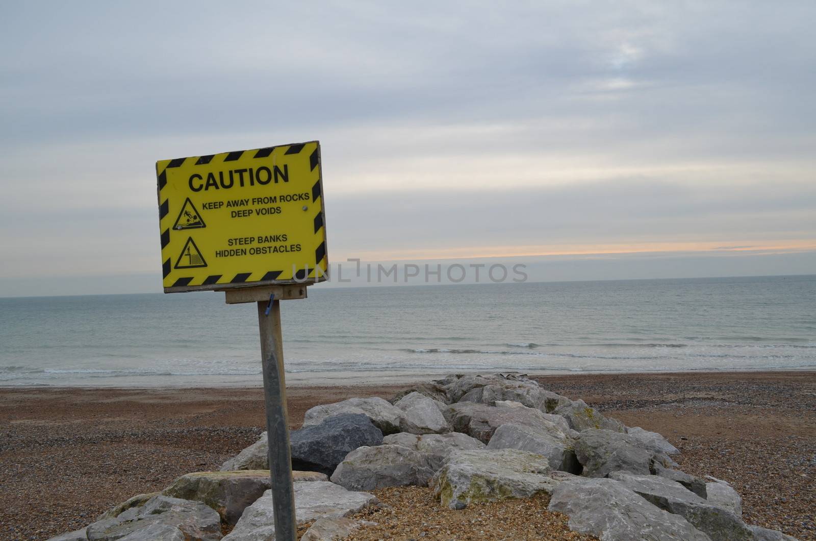 A yellow information sign warning of rocks and hidden objects along the seashore.Image taken along Worthing beach,Sussex,England.
