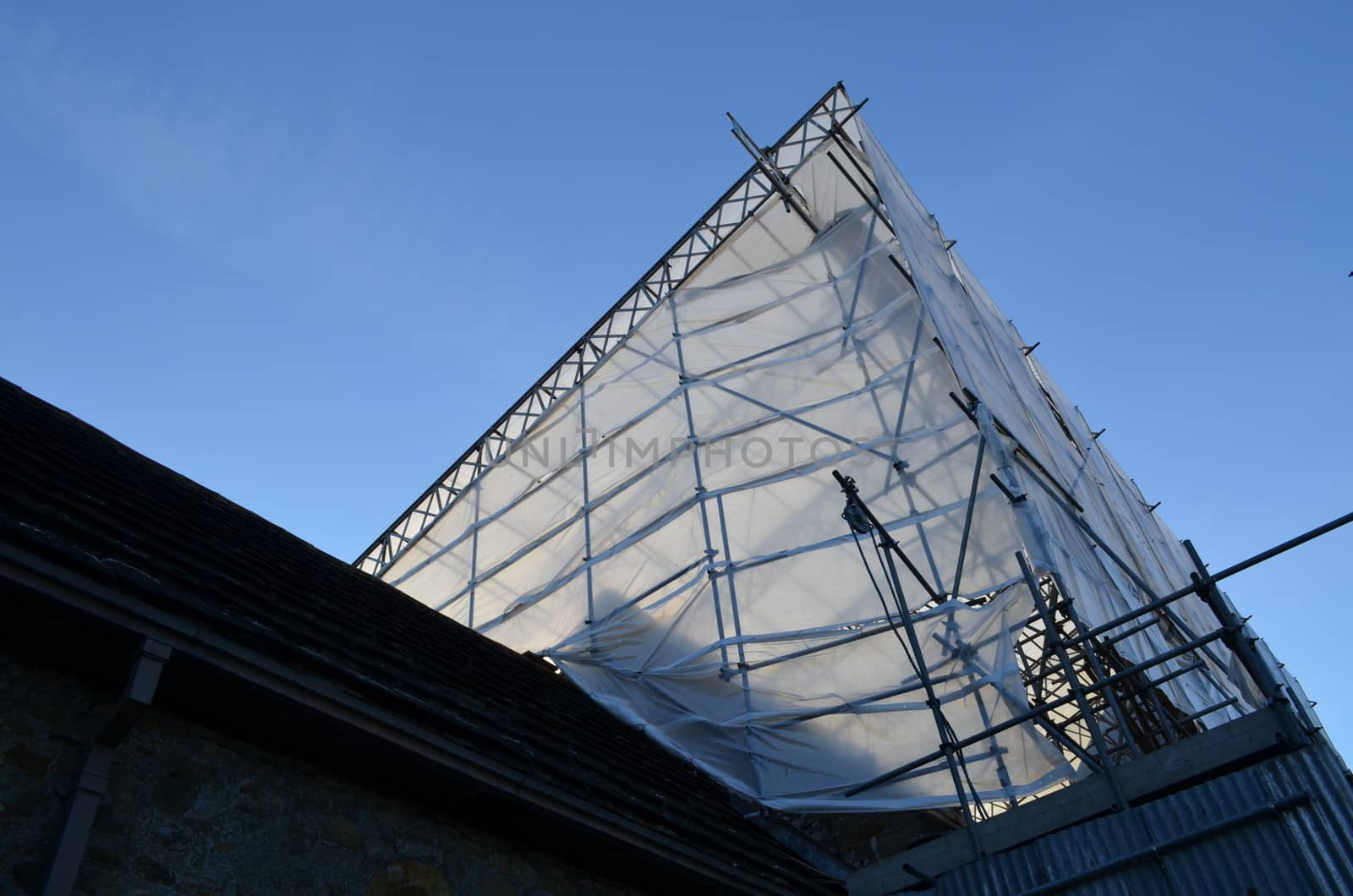 A building being renovated under a framework of metal scaffolding and plastic sheeting.