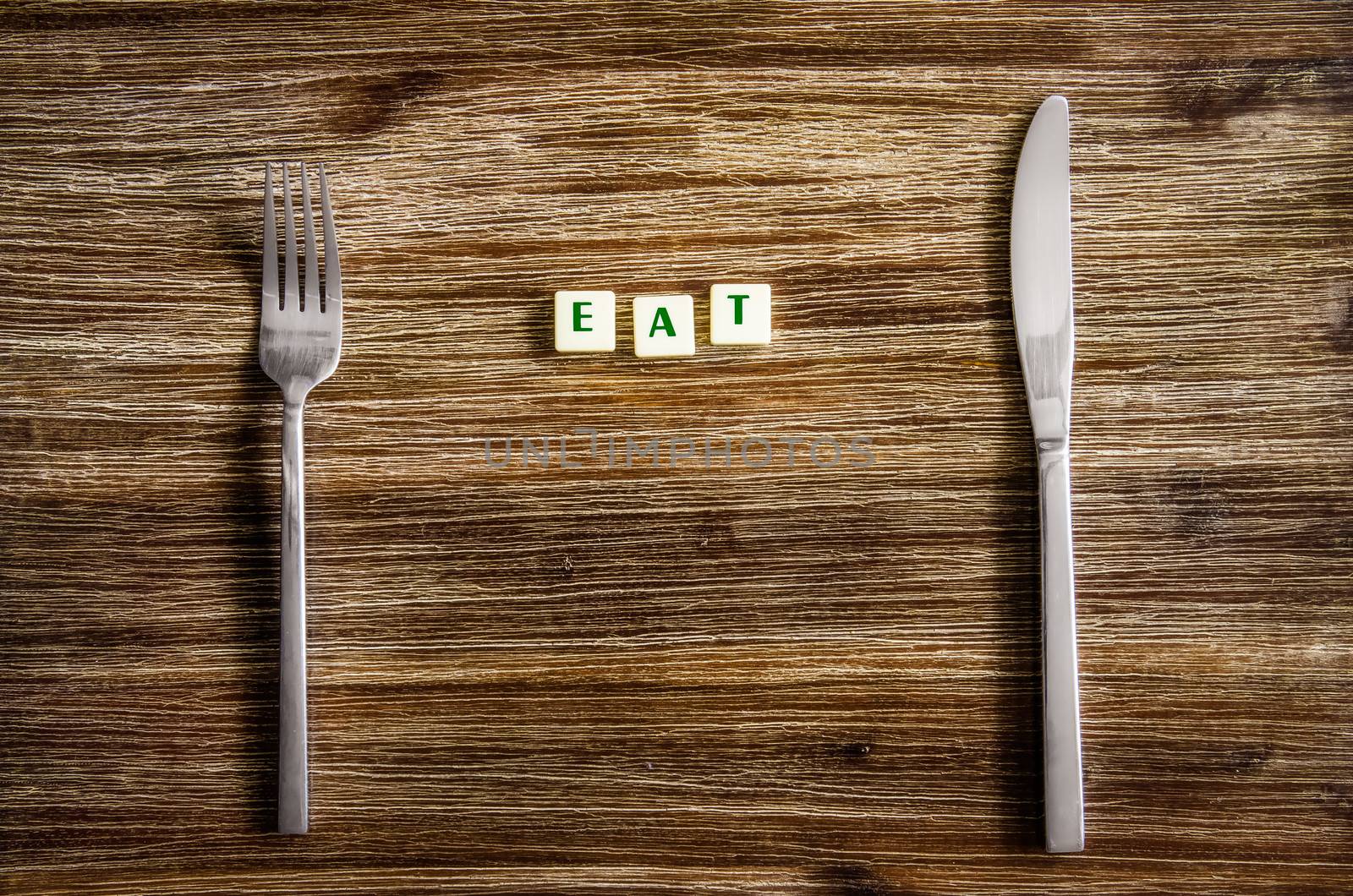 Knife and fork set on a wooden vintage table with sign Eat