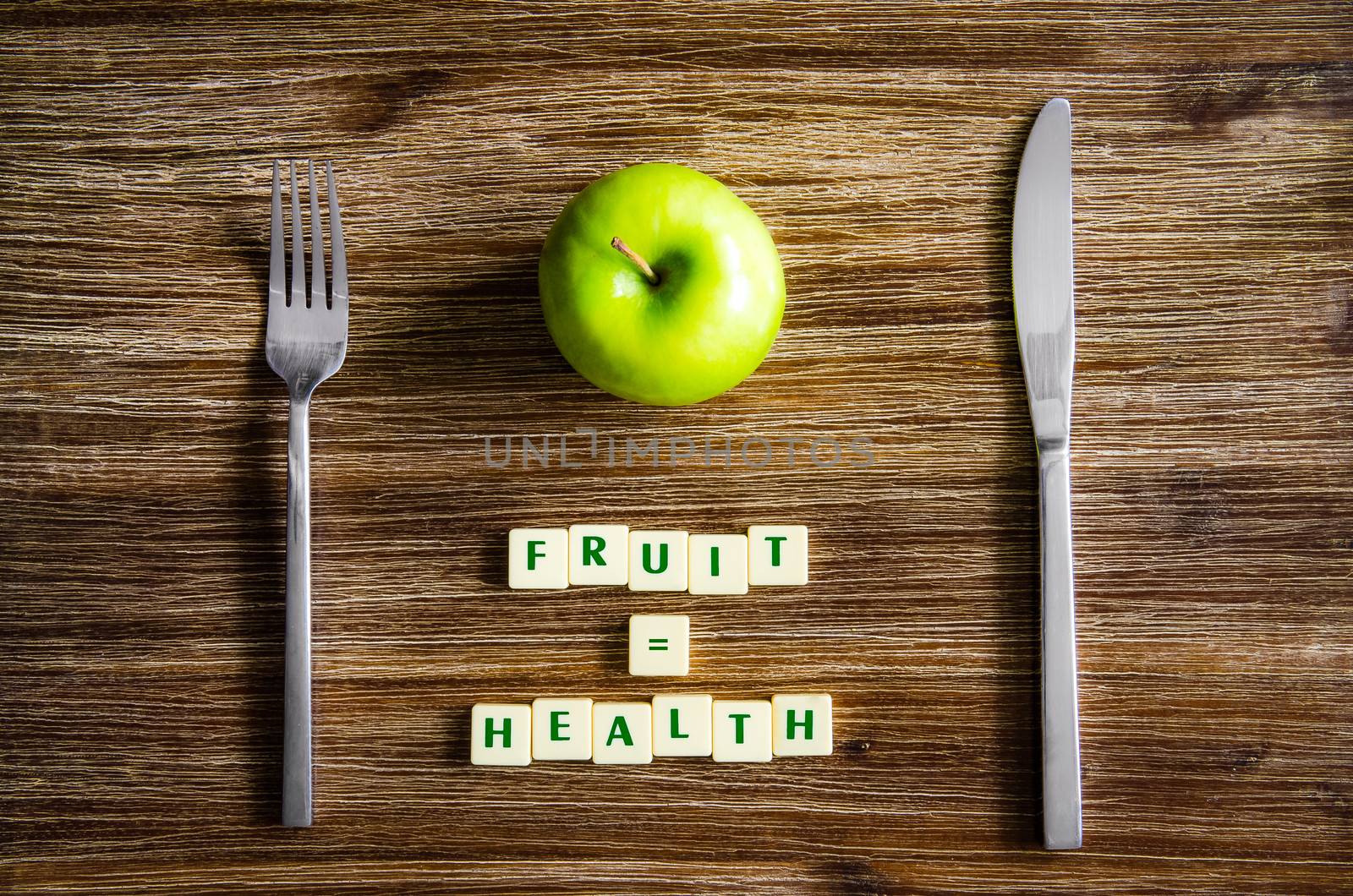 Silverware and apple set on wooden table with sign saying Fruit equals health