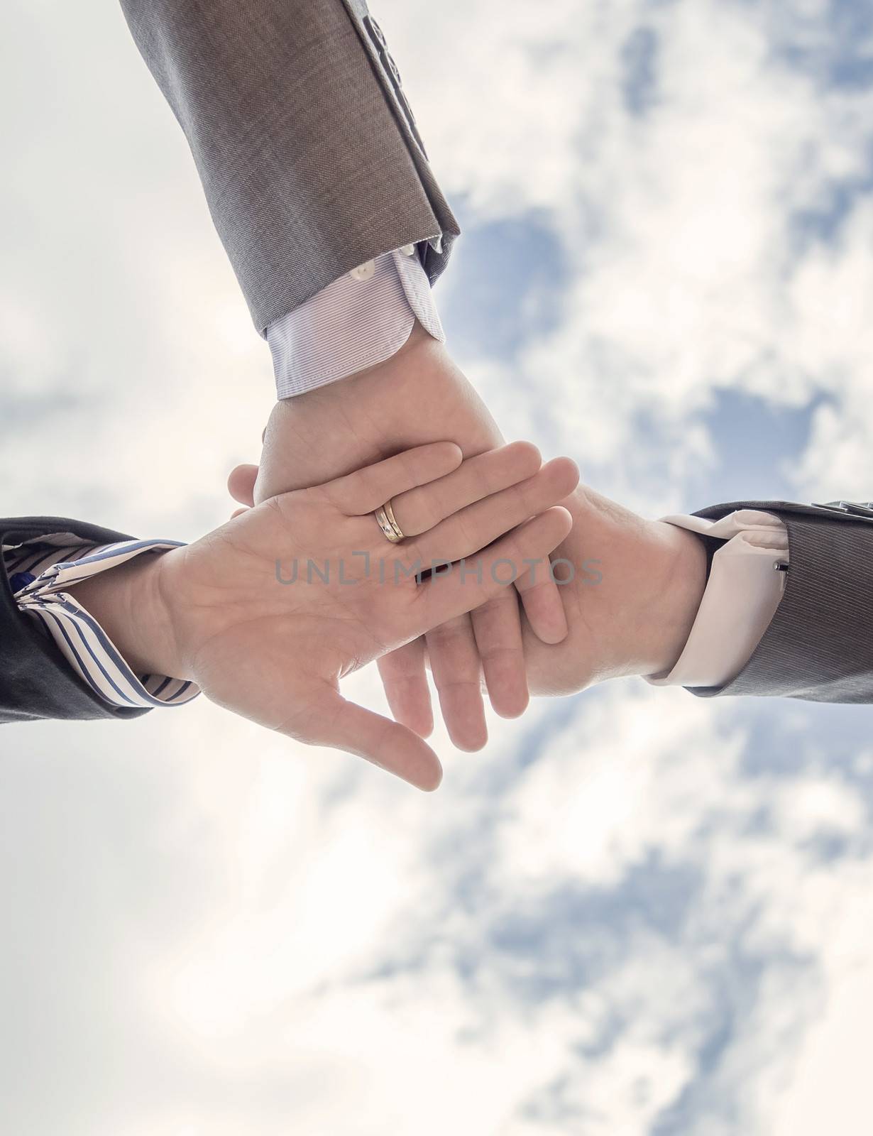 Bottom view of business team showing unity with hands together over blue sky background