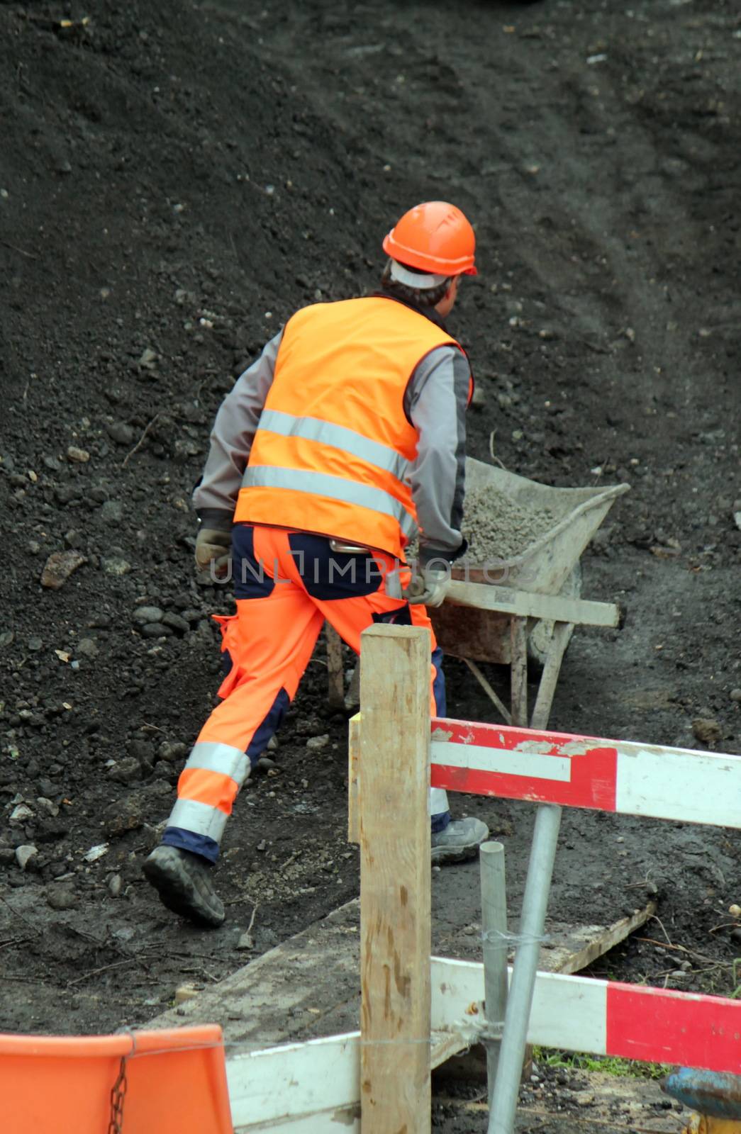 Worker wearing orange uniform pushing wheelbarrow on the construction site