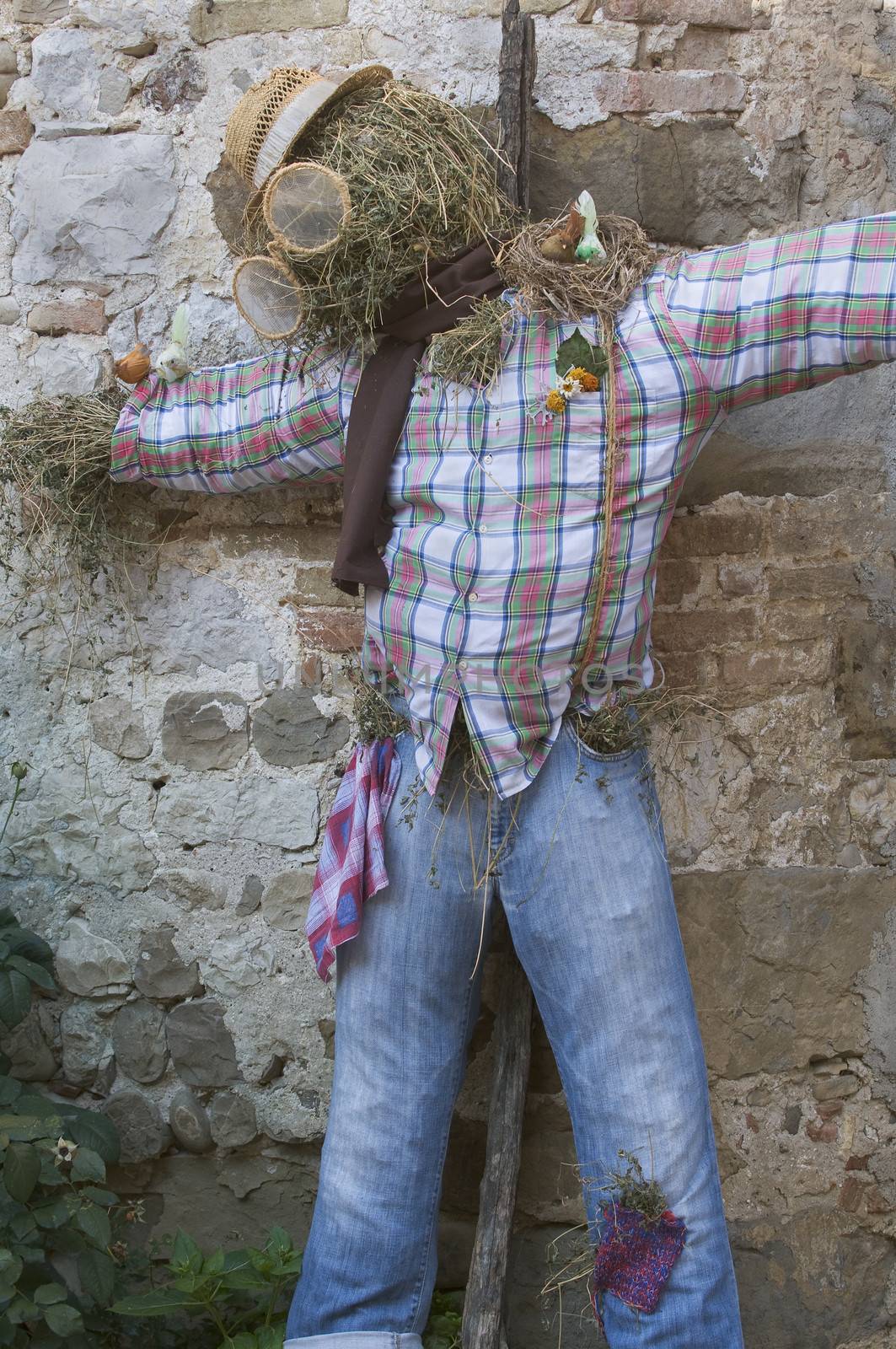 Traditional decoration of stray scarecrow wearing jeans and squared shirt against a stone wall