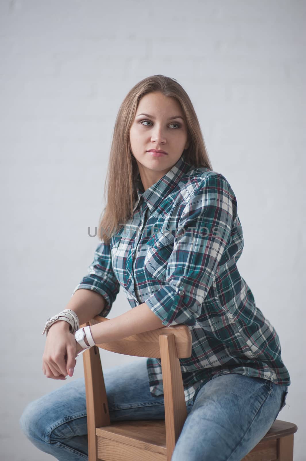 beautiful girl dressed in jeans and a shirt poses sitting on a chair