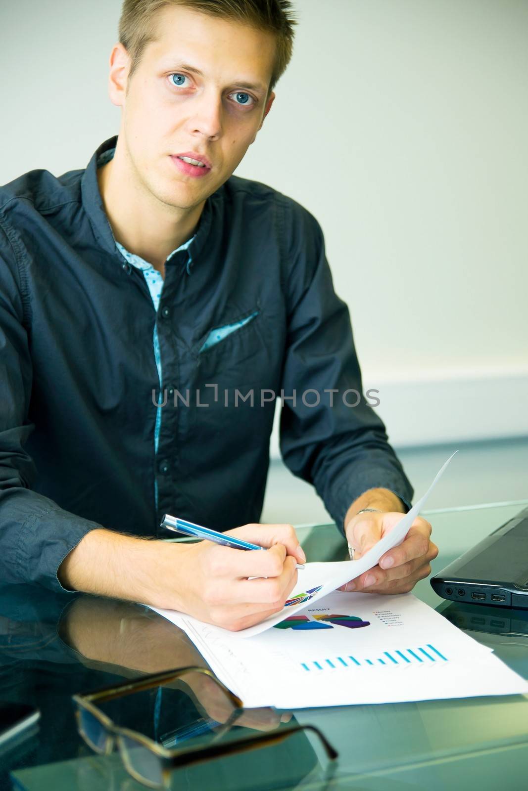 Young businessman sitting at table and working with charts
