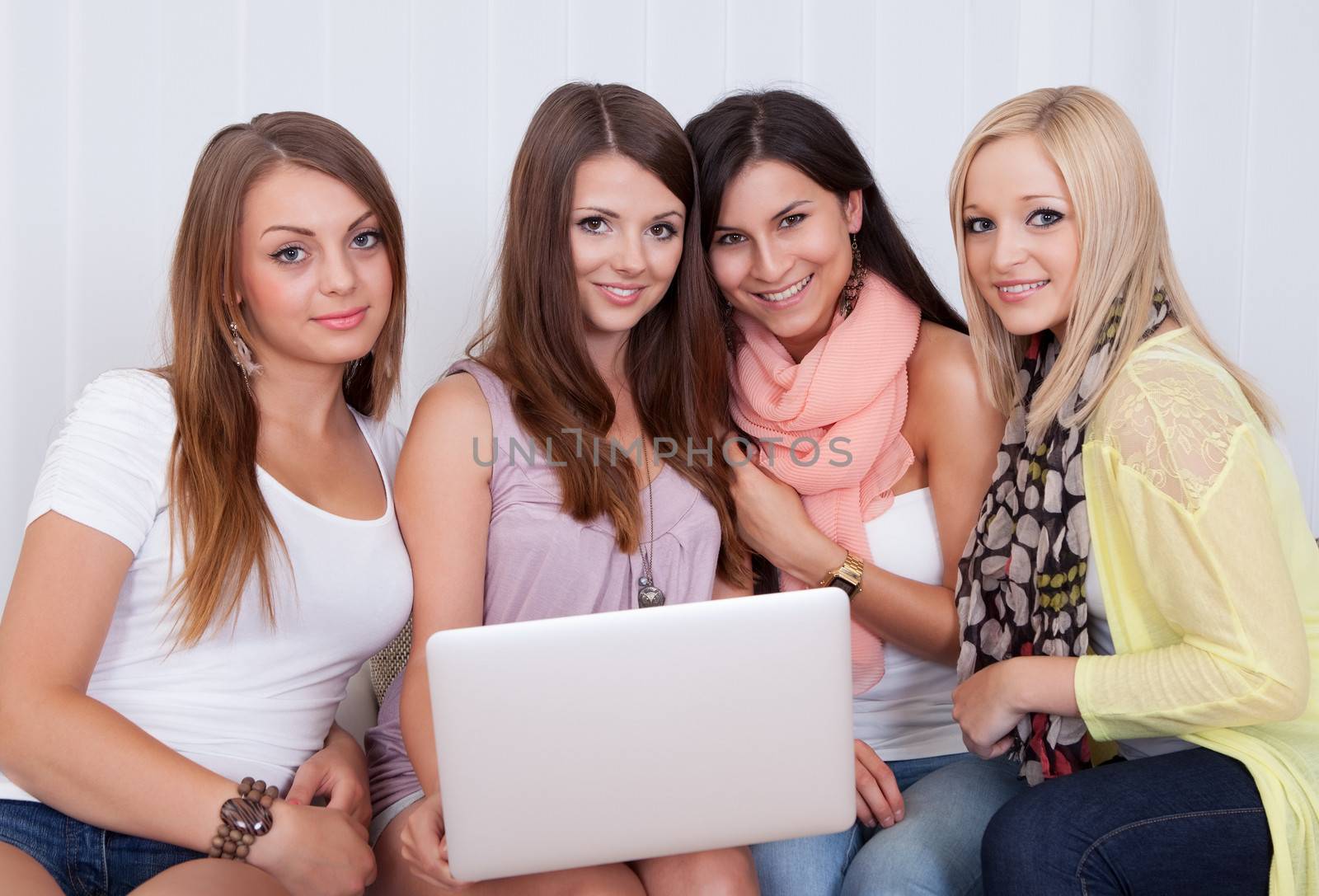 Group of beautiful young women sitting together on a couch sharing a laptop and smiling at something on the screen