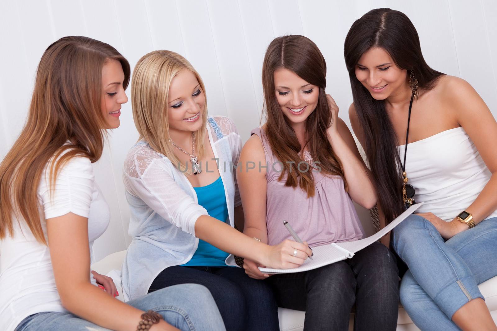 Four elegant beautiful female friends sit on a couch with their heads close together looking at a folder