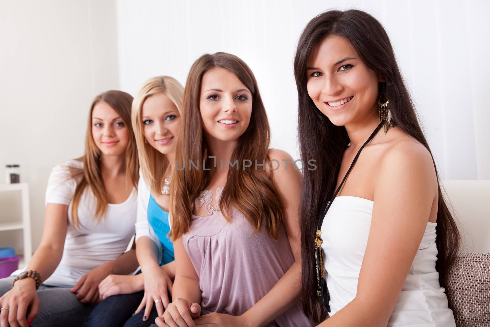 Row of beautiful stylish young ladies sitting on a couch in a living room