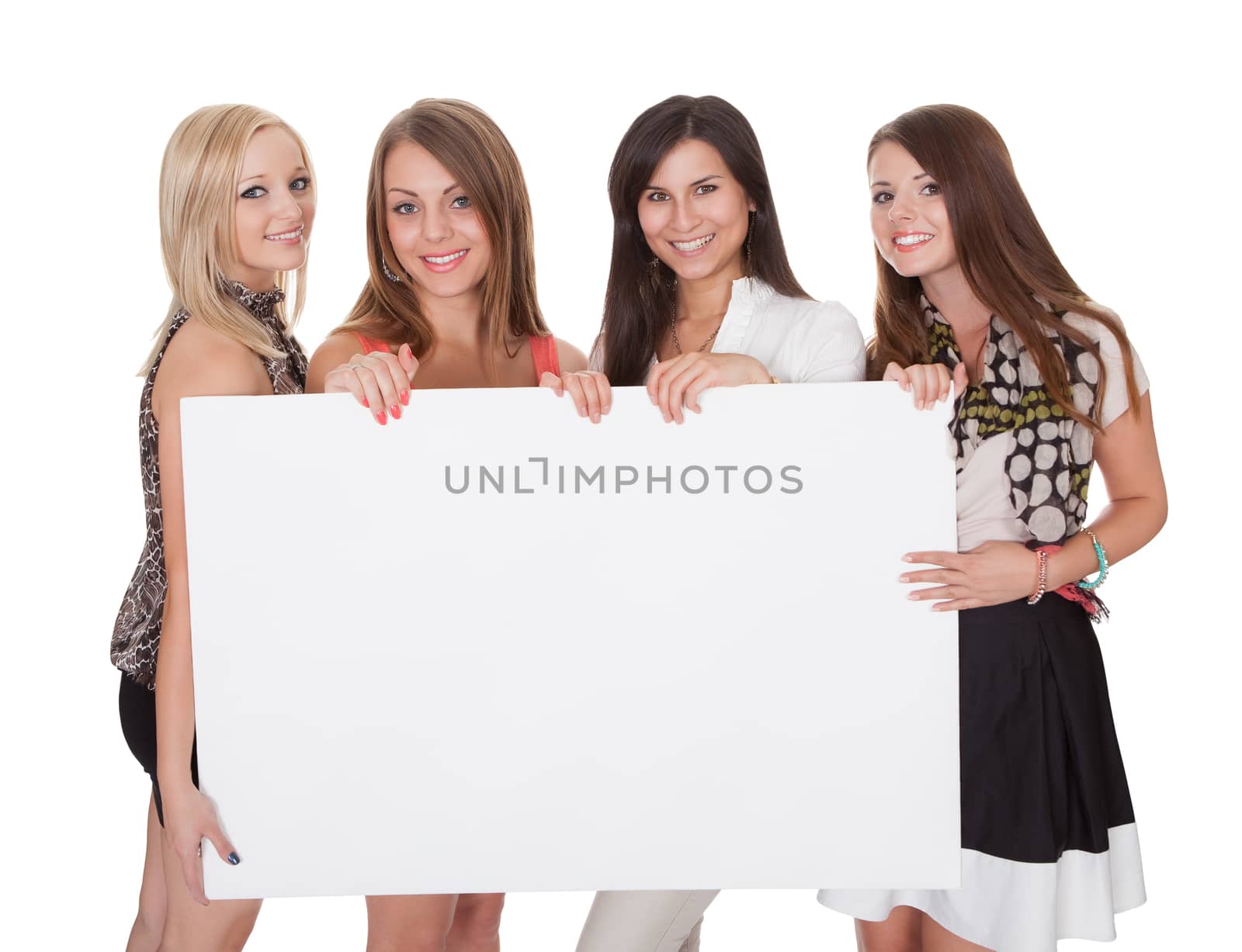 Four attractive smiling young women with a blank white sign with copyspace for your text