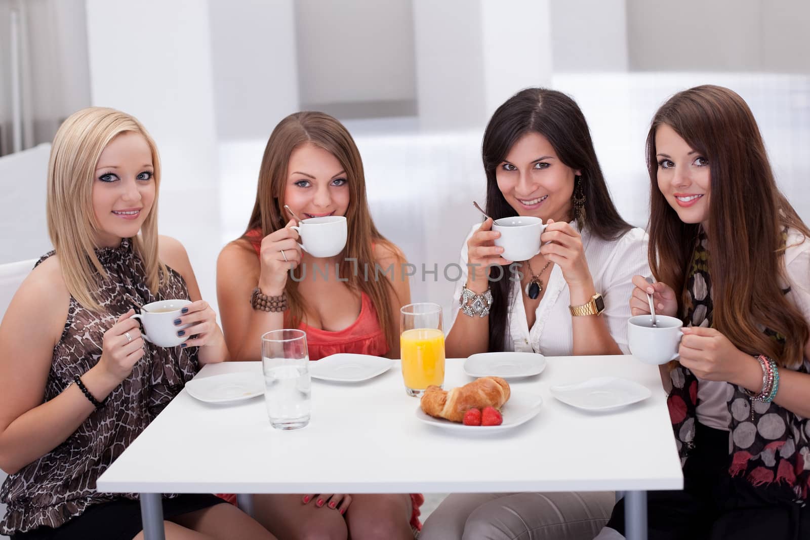 Four stylish attractive young female friends seated at a table chatting over coffee