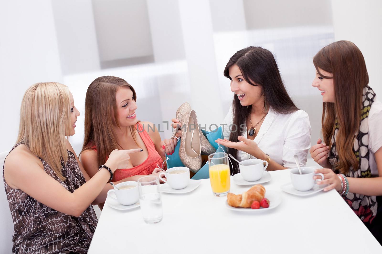 Women discussing footwear together seated at a morning coffee table as they compare their shopping purchases