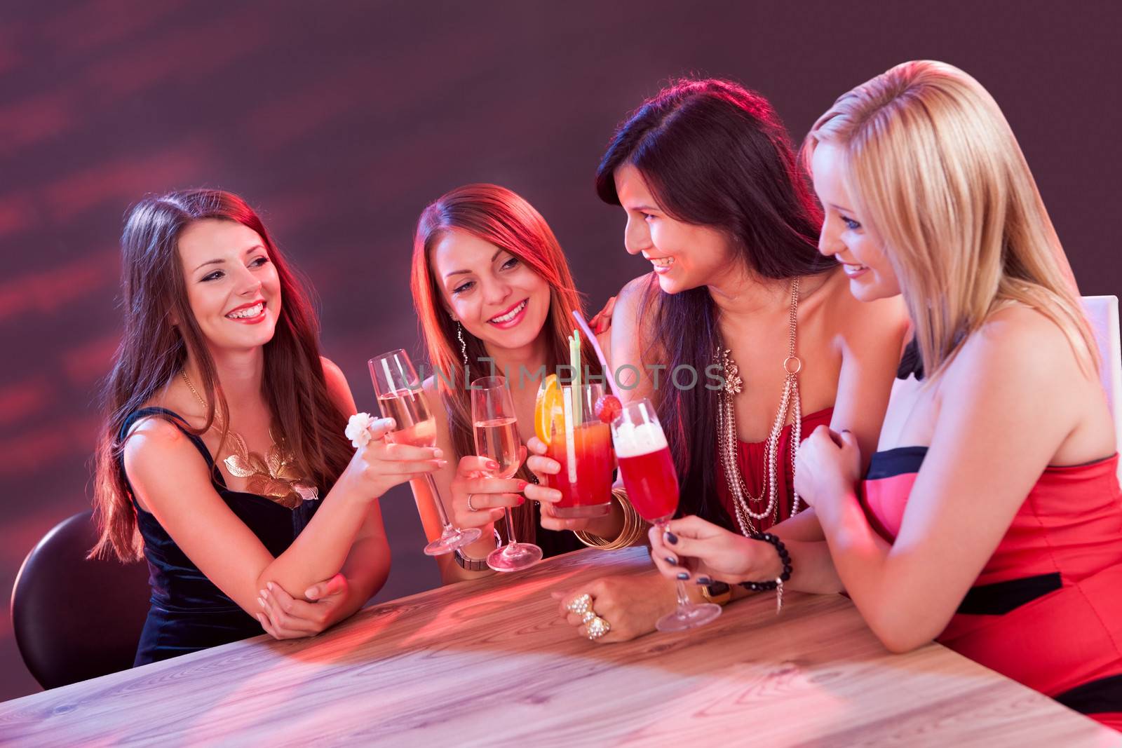 Female friends enjoying a night out sitting having cocktails at a table in a nightclub