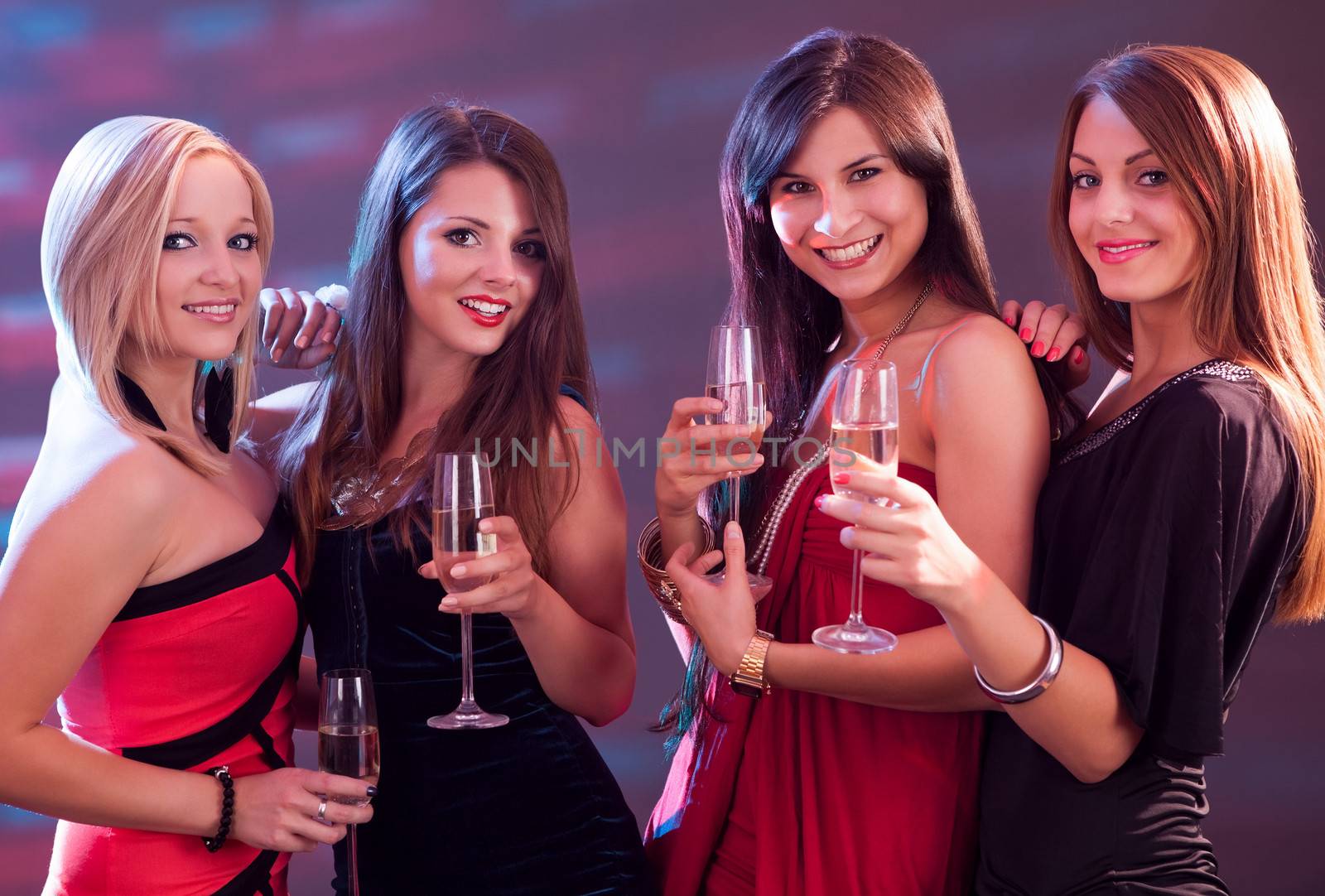 Group of four stylish women standing in a row toasting with flutes of champagne