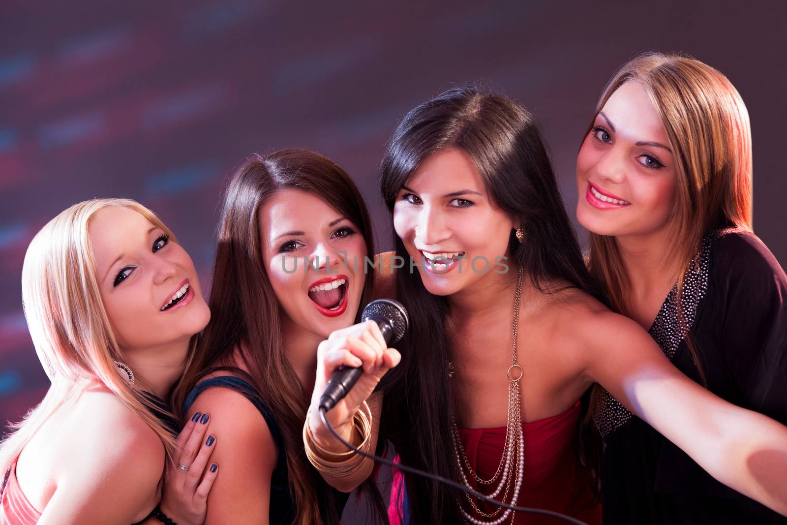 Four beautiful stylish girls singing karaoke at the club