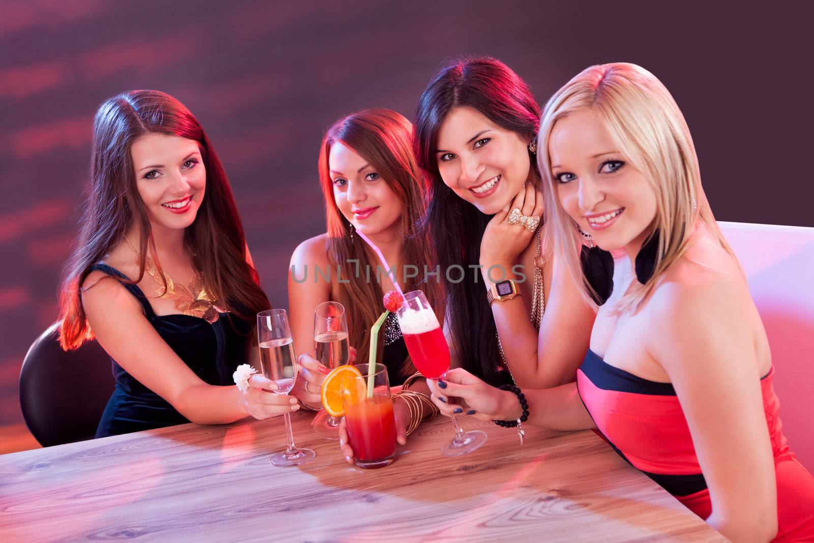 Female friends enjoying a night out sitting having cocktails at a table in a nightclub