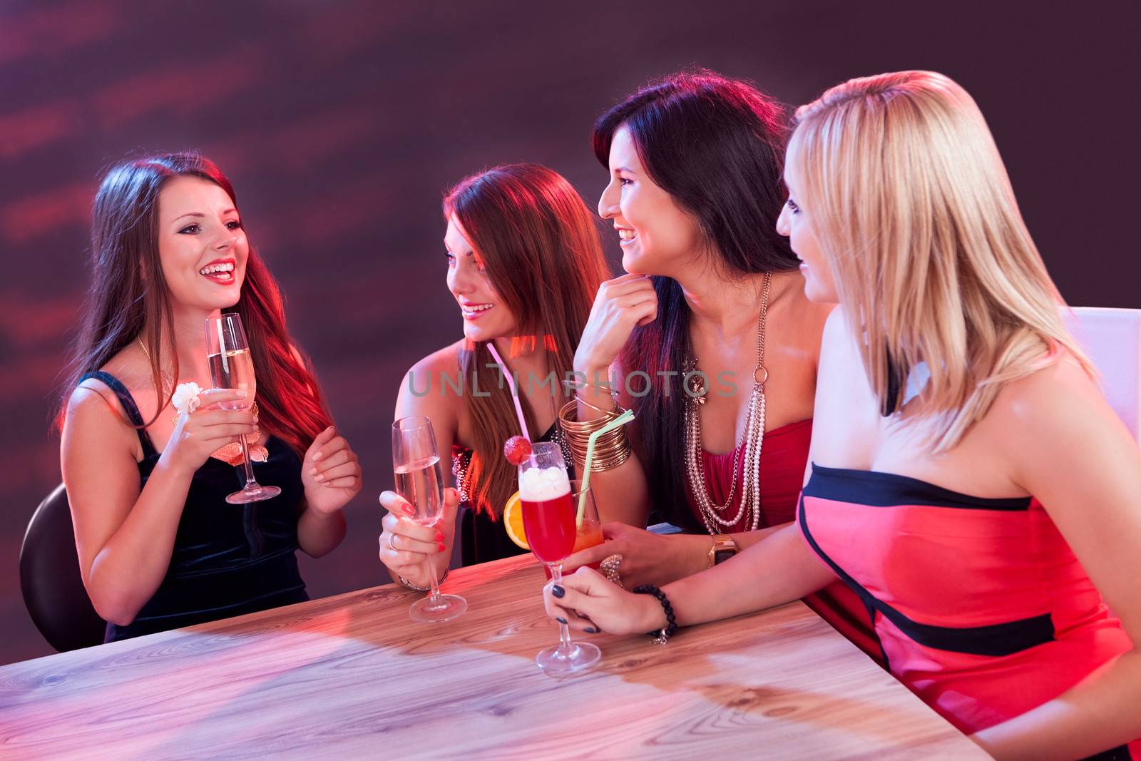 Female friends enjoying a night out sitting having cocktails at a table in a nightclub