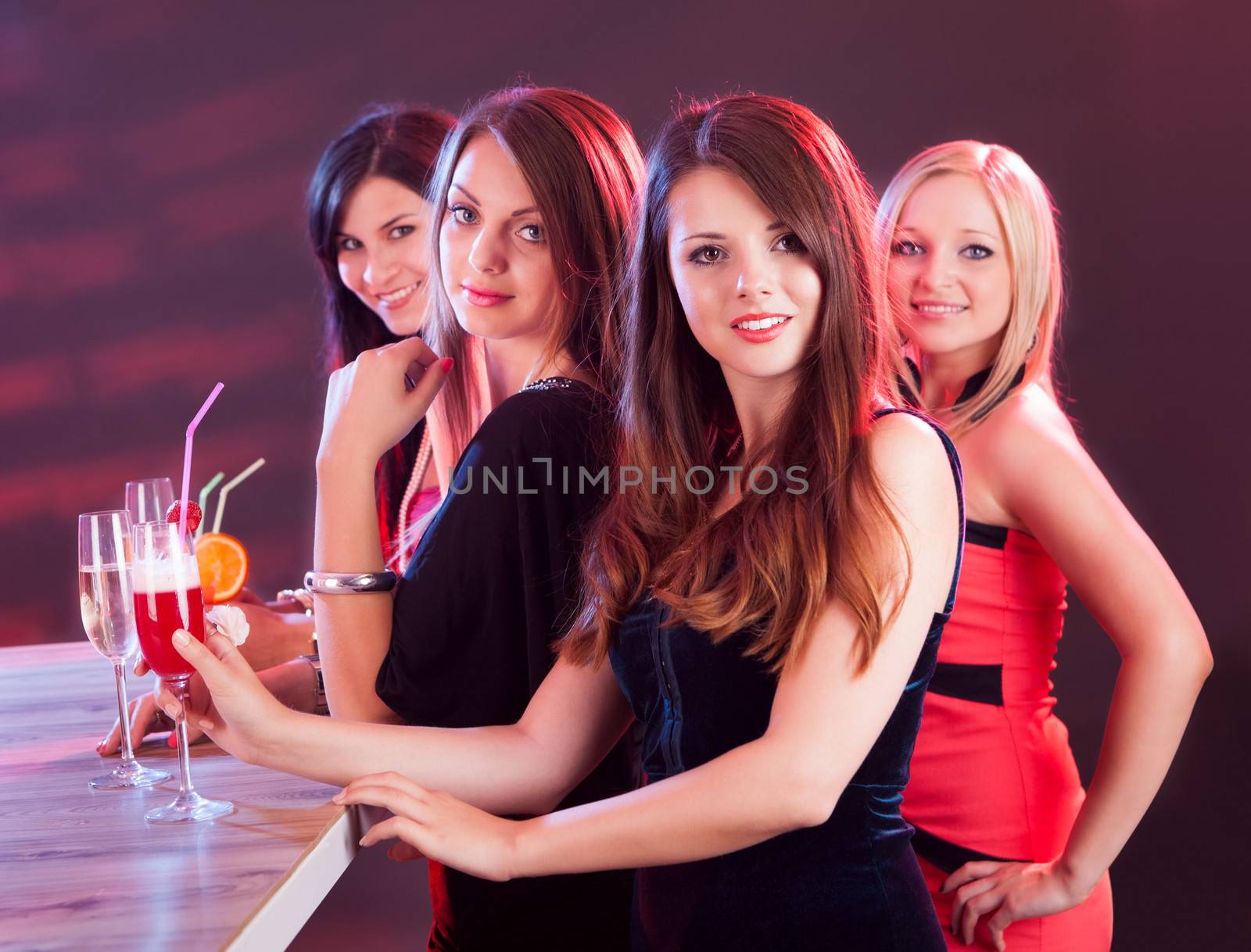 Four beautiful fashionable women on a night out standing at a bar counter with their drinks