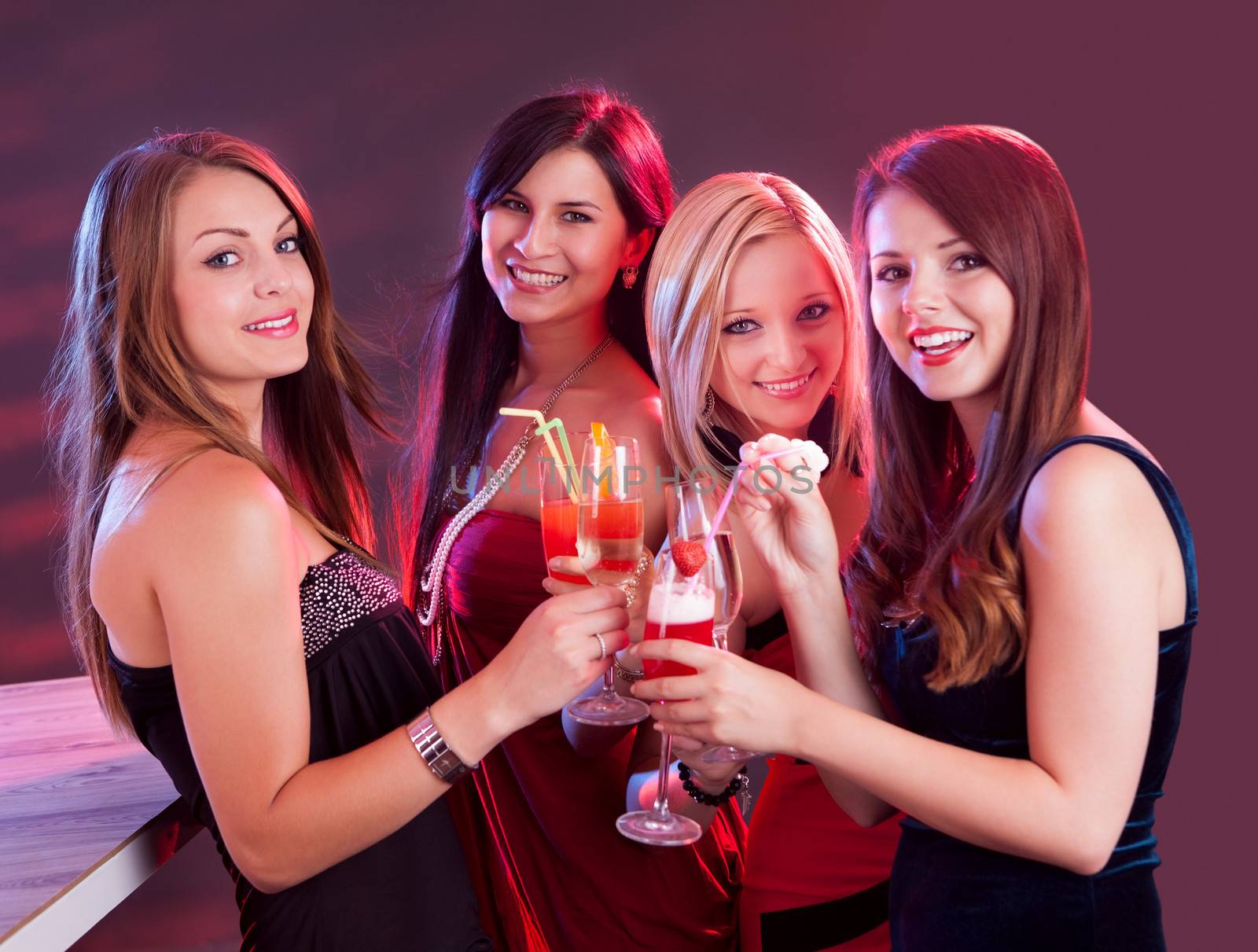 Group of four happy beautiful young female friends celebrating in a nightclub with glasses of cocktail in their hands
