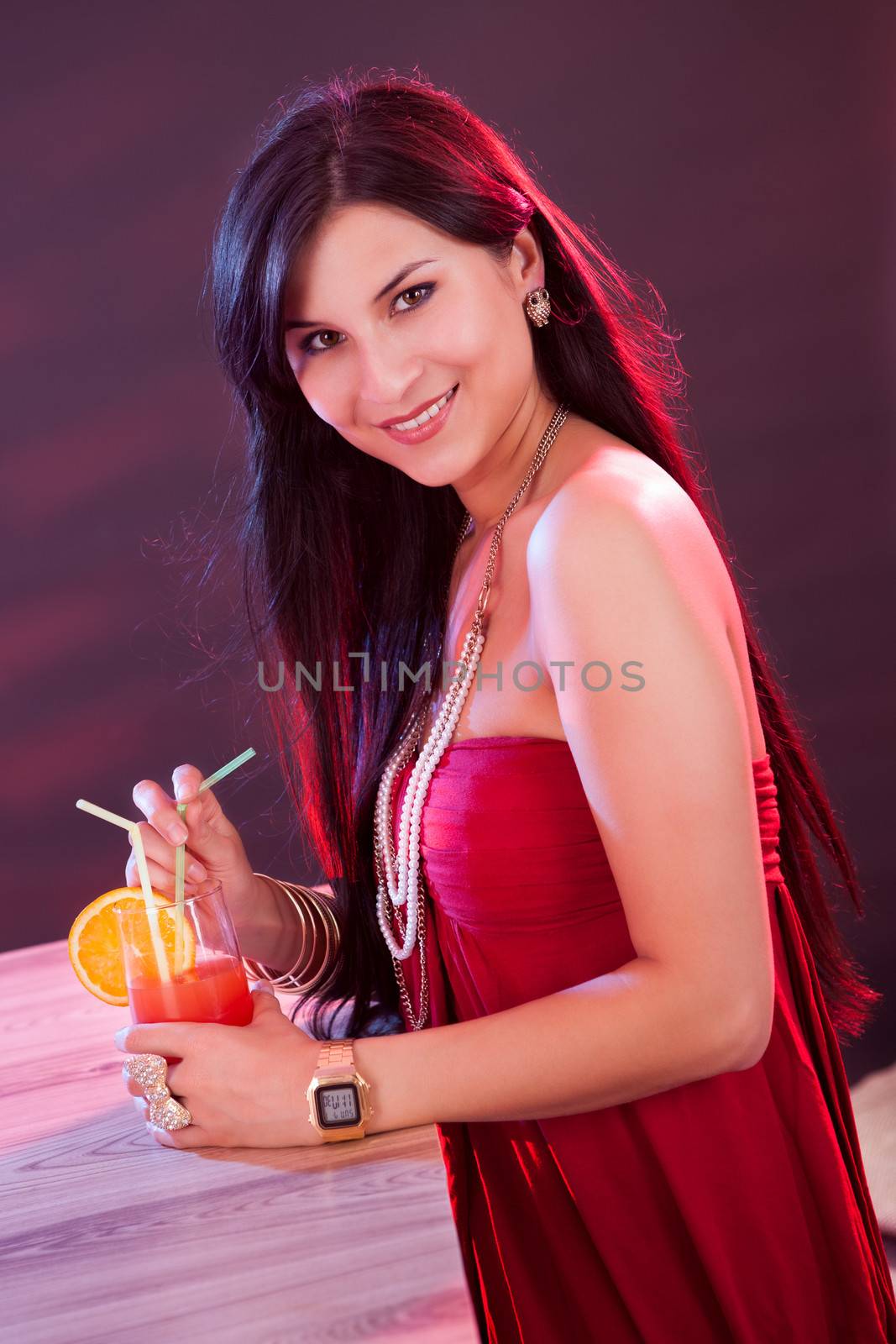Glamorous beautiful woman in an evening dress holding a cocktail in her hand while standing at the bar in a nightclub