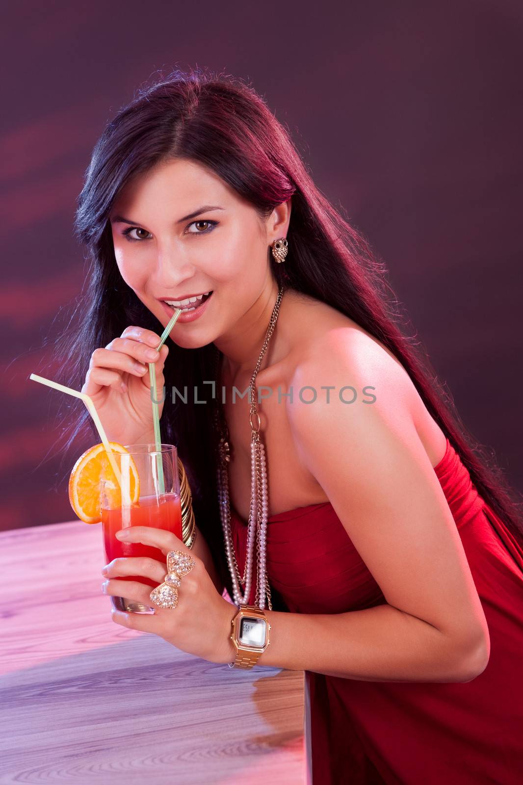 Glamorous beautiful woman in an evening dress holding a cocktail in her hand while standing at the bar in a nightclub