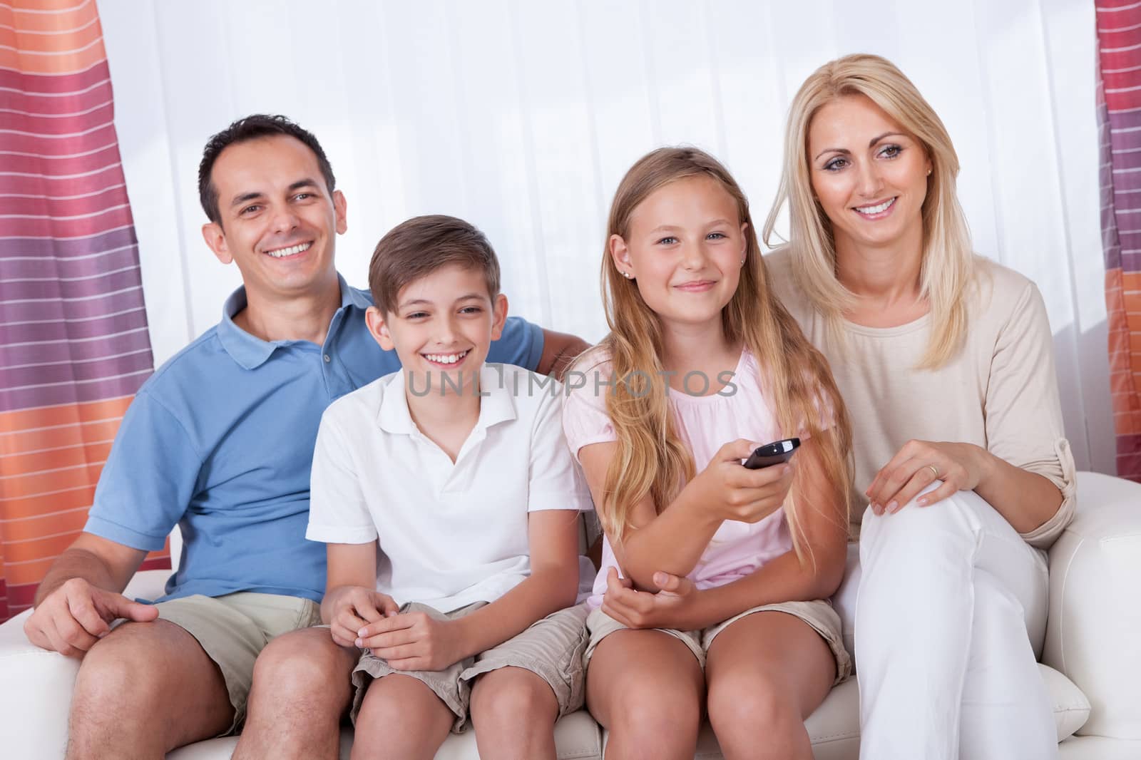 A Happy Family With Two Children Sitting On A Sofa Watching Tv At Home