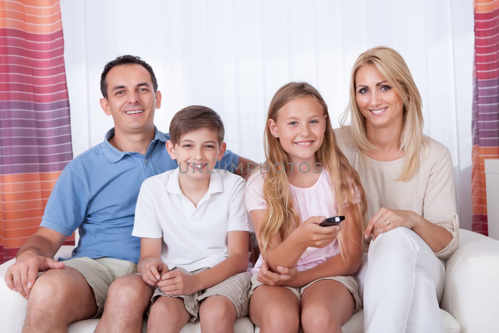 A Happy Family With Two Children Sitting On A Sofa Watching Tv At Home