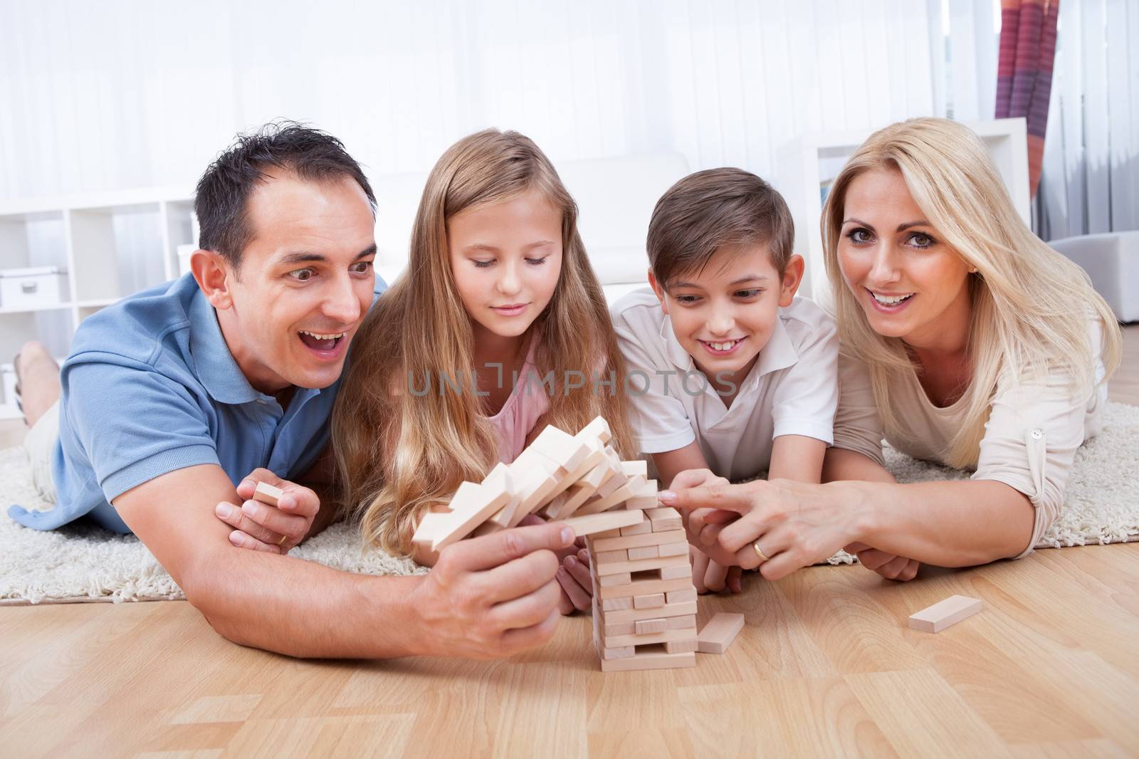 Happy Family With Two Children Collapsing The Wooden Blocks At Home