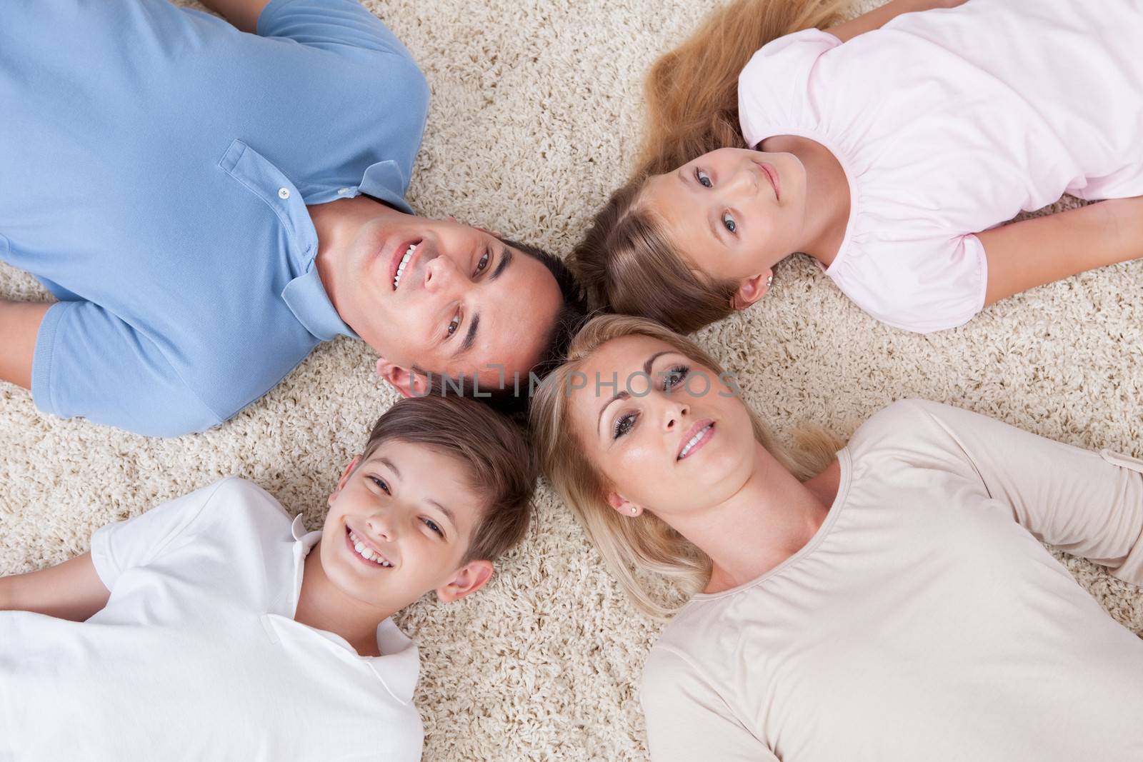 Close-up Of Happy Family Lying On Carpet Looking Up Heads Together At Home