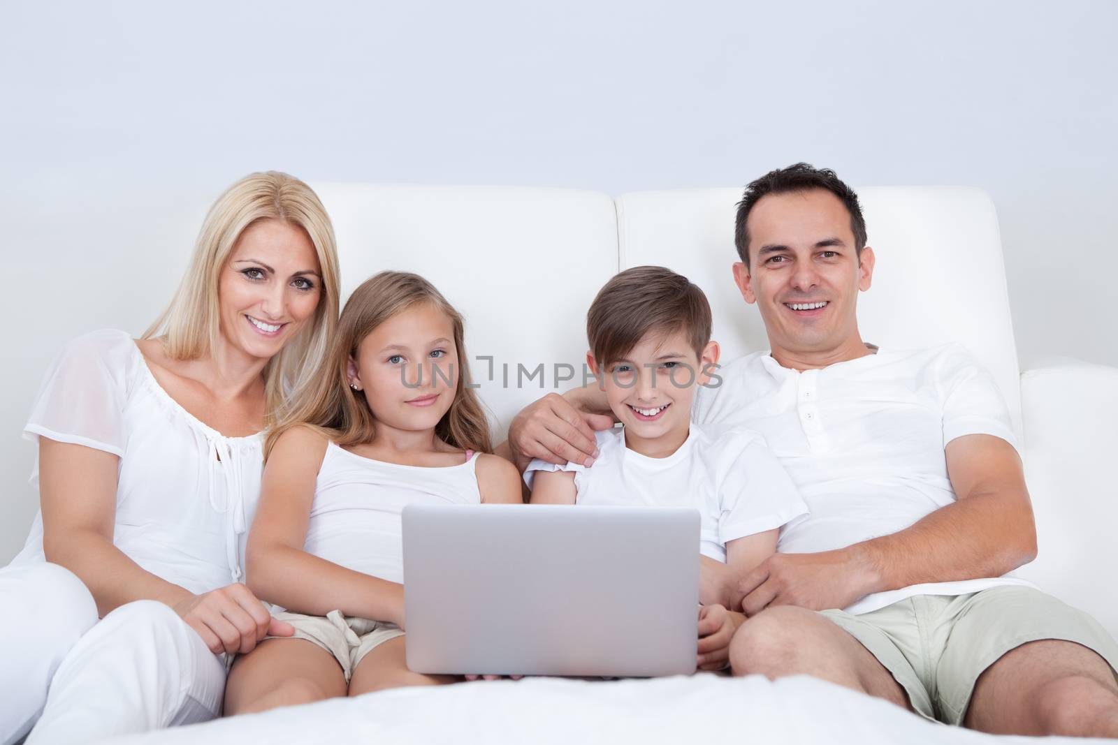 Portrait Of Happy Family With Two Children Sitting On Bed In Bedroom