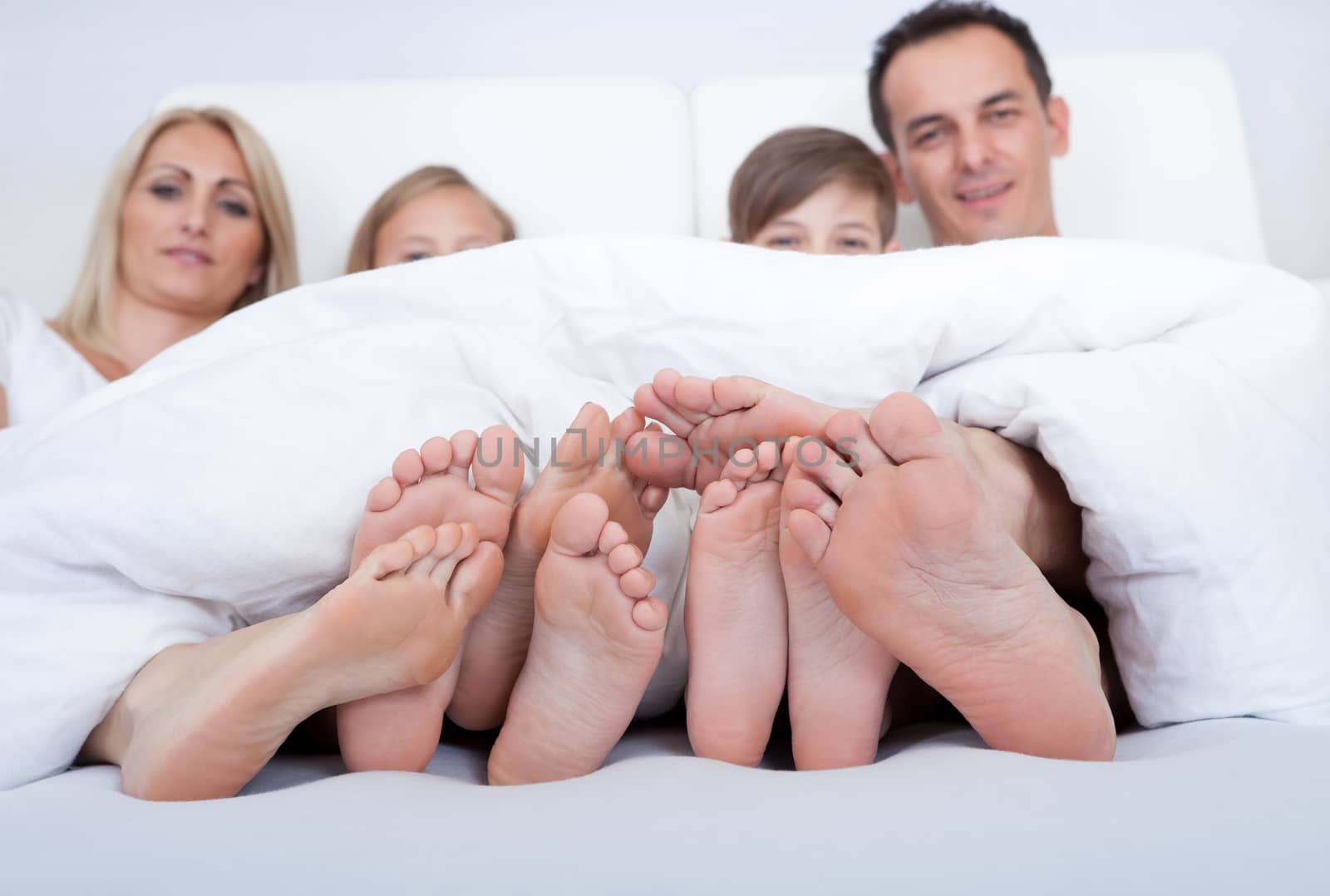 Happy Family With Two Children In Bed Under Cover Showing Feet, Indoors