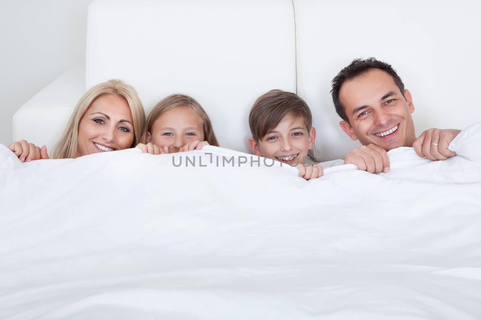 Happy Family With Two Children In Bed Under Cover, Indoors