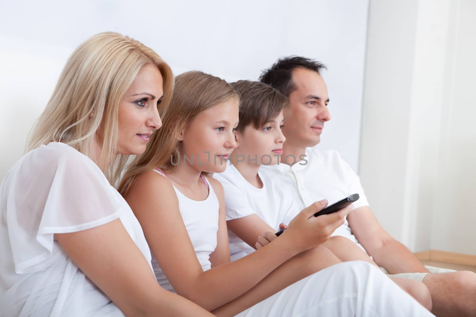 A Happy Family With Two Children Sitting In Bed Watching Tv At Home