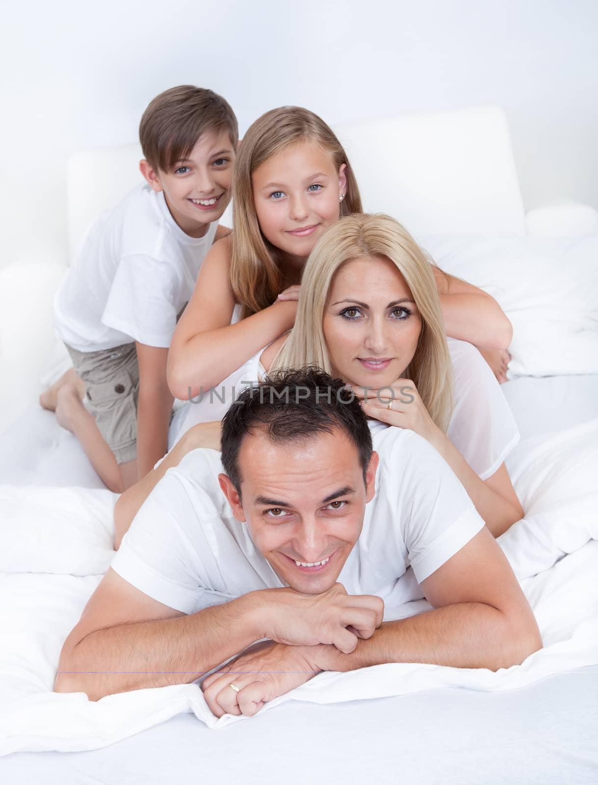 Happy Family With Two Children Lying Heaped On Bed At Home