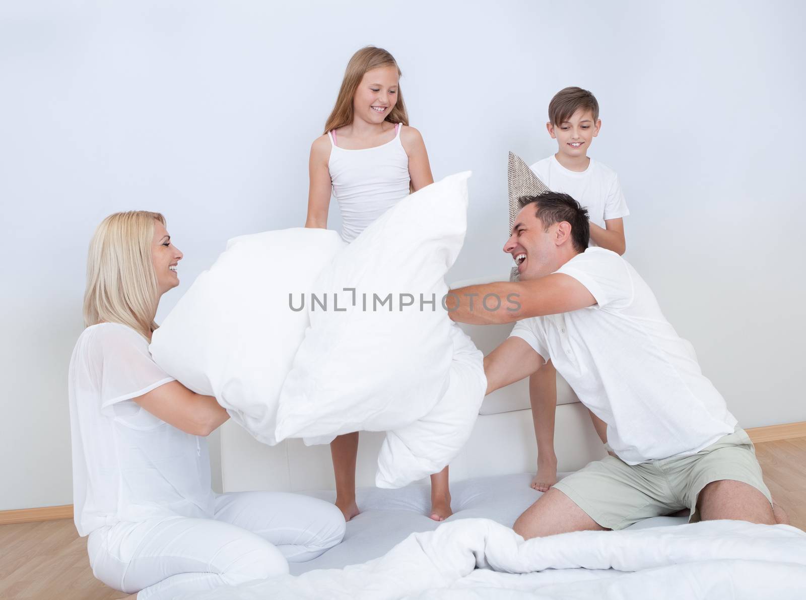 Playful Family Having A Pillow Fight Together On Bed In Bedroom