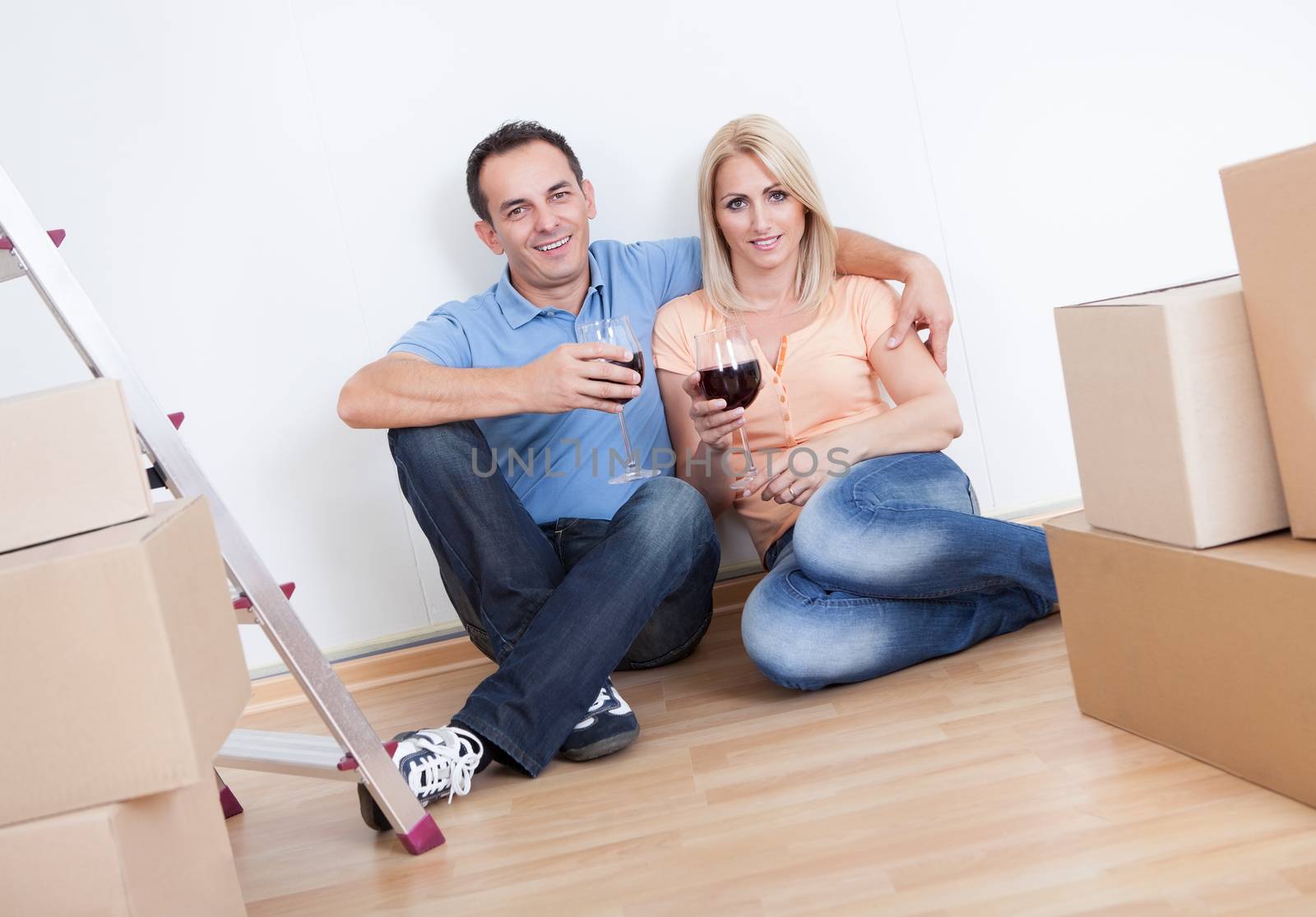 Couple Sitting Between Cardboard Boxes And  Holding Wine Glass, Indoors