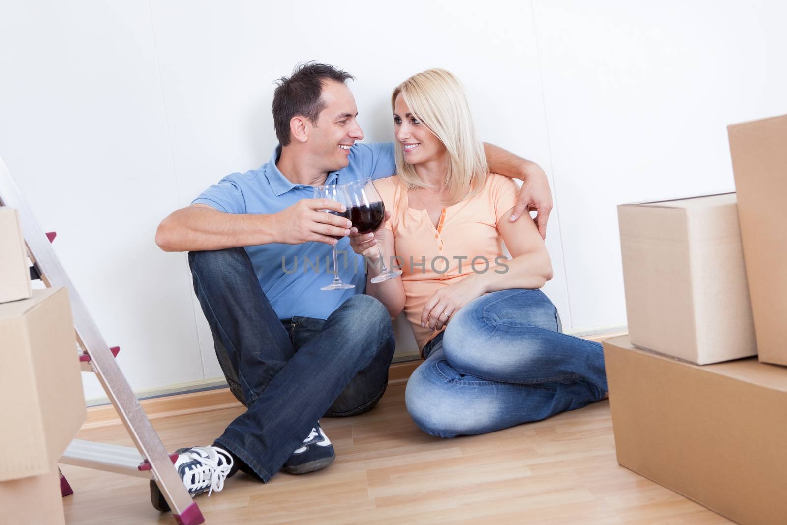 Couple Sitting Between Cardboard Boxes And  Holding Wine Glass, Indoors