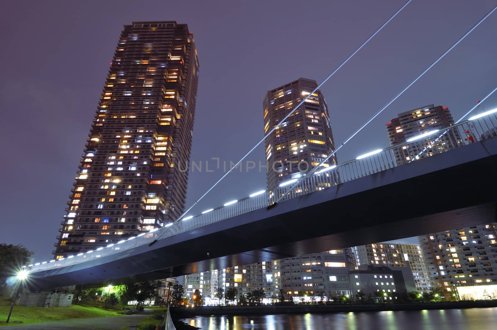 huge residential skyscrapers with illuminated windows beyond illuminated suspension bridge structure in Tokyo, Japan