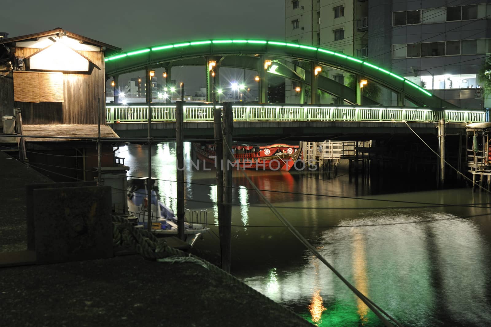 traditional Japanese red boat under modern illuminated bridge inside one of waterway channels in Tokyo, Japan