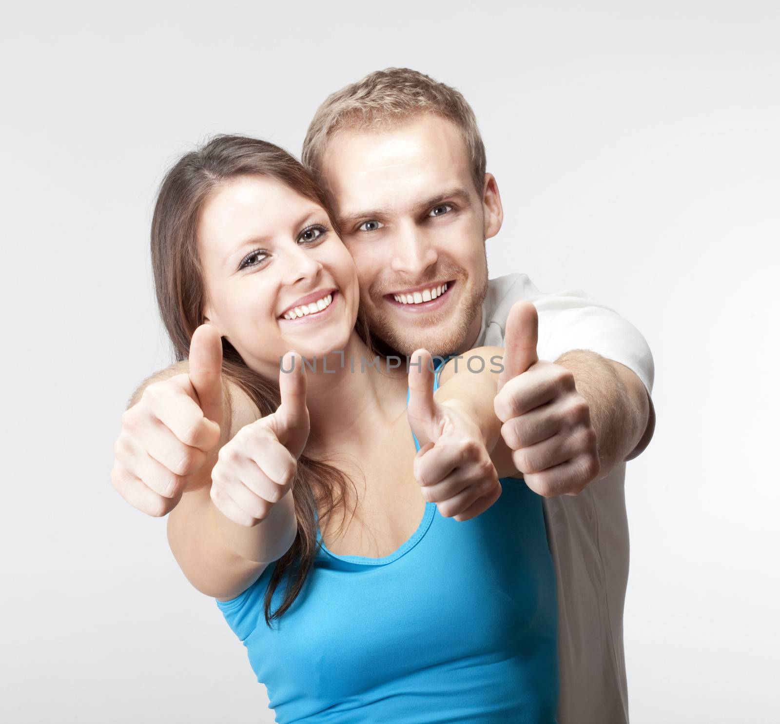 young couple showing both thumbs up smiling- isolated on gray