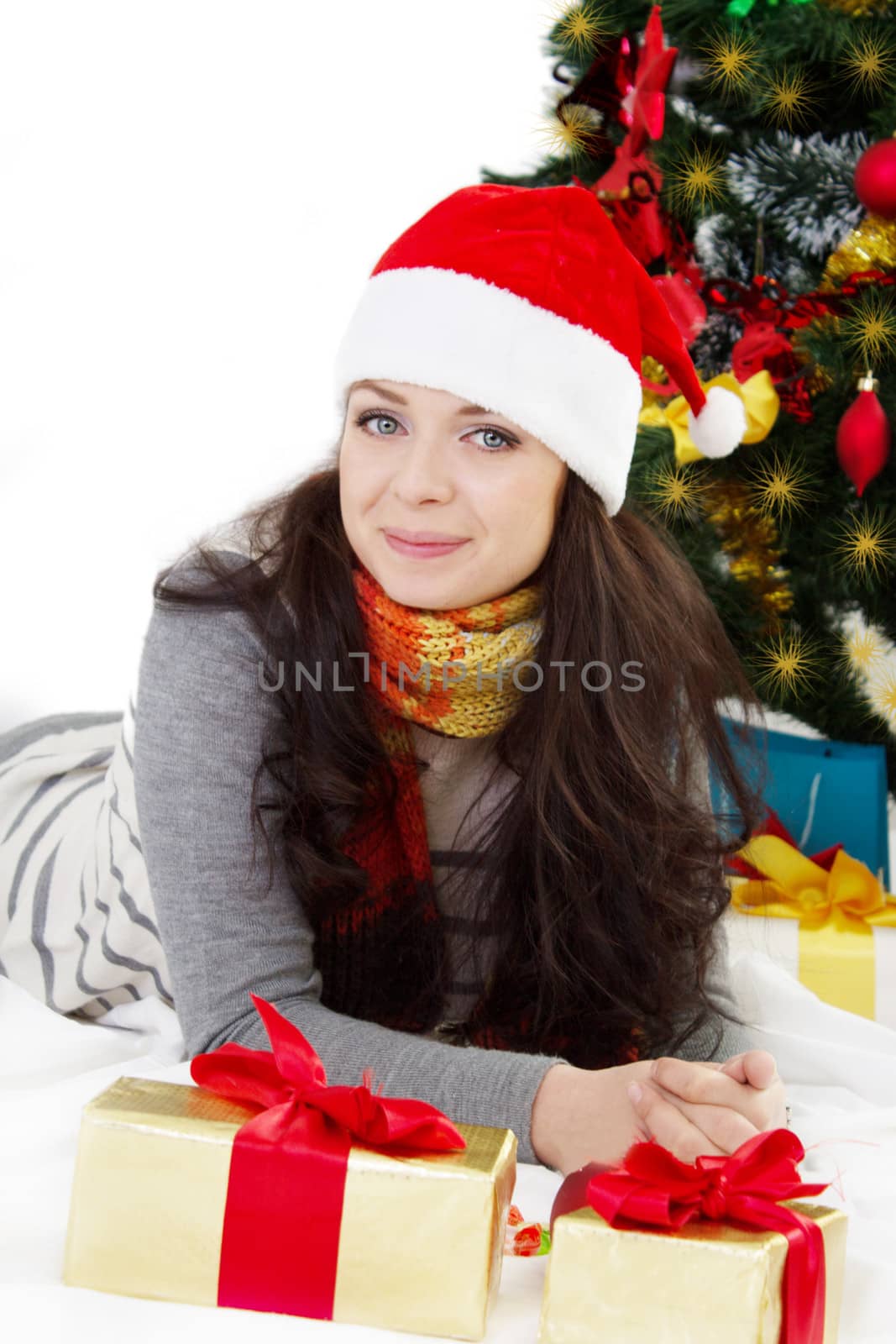 Smiling woman in Santa hat lying under Christmas tree over white