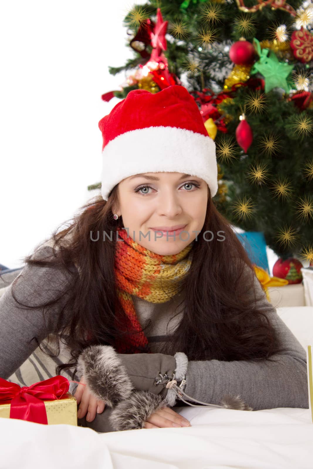 Smiling woman in Santa hat and fur mittens lying under Christmas tree