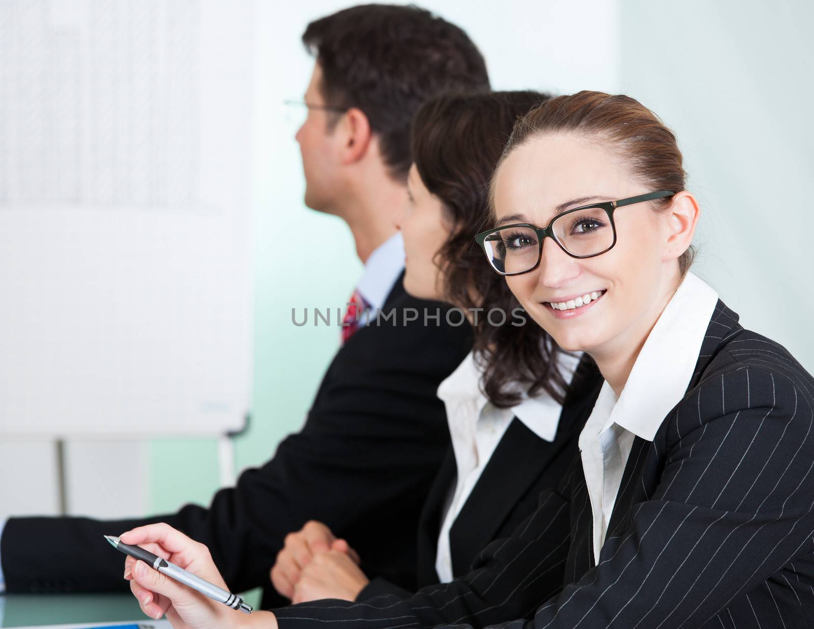 Smiling successful businesswoman wearing glasses looking at the camera while seated in a meeting with her colleagues